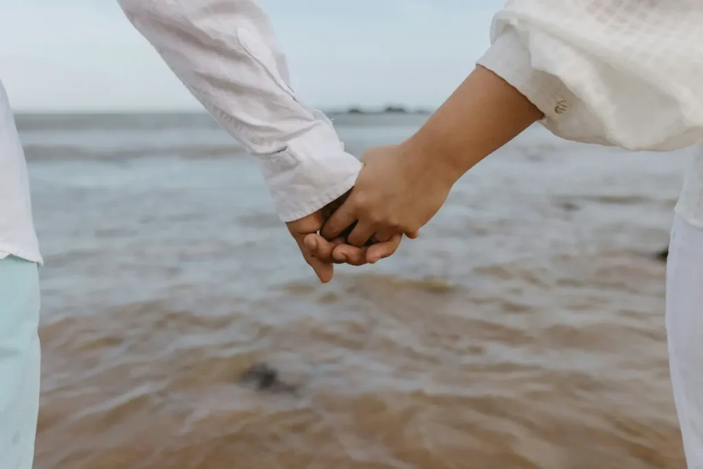 Casal de mãos dadas na beira do mar.